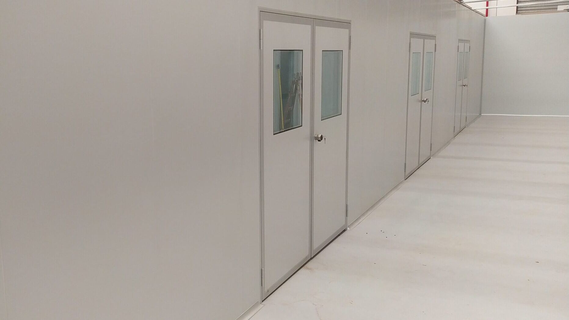 Pasillo de sala limpia con tabiques sanitarios y puertas de doble contacto con visor